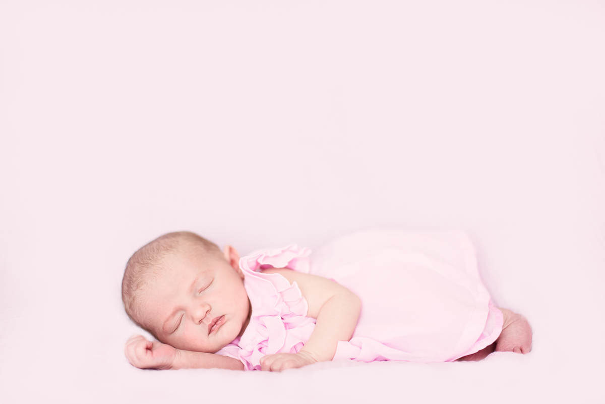 Baby girl in a pink dress laying on her side.