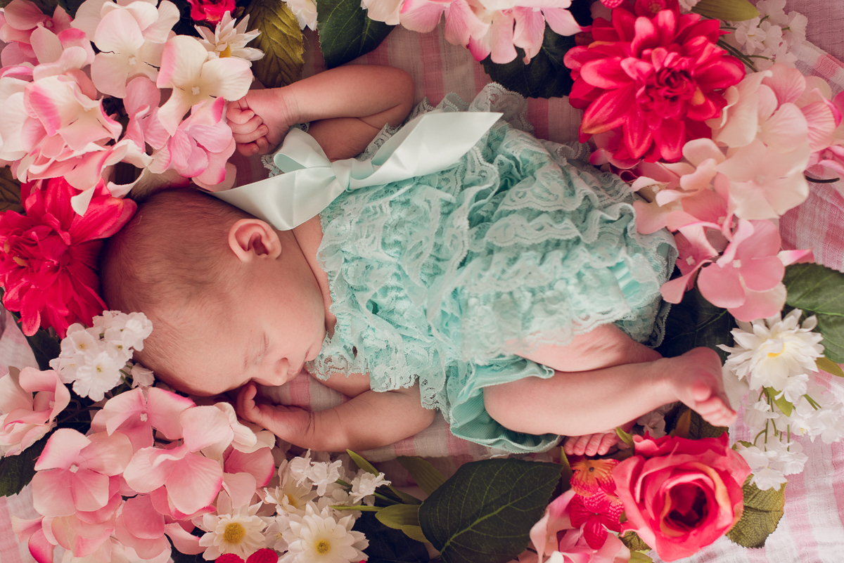 Baby girl wearing a green dress laying in a bed of pink flowers.